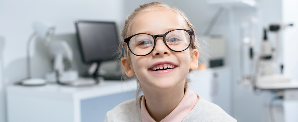 Little girl smiling at camera with big glasses inside of a clinic for an eye test