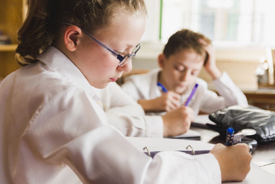 Child writing on paper with glasses in school