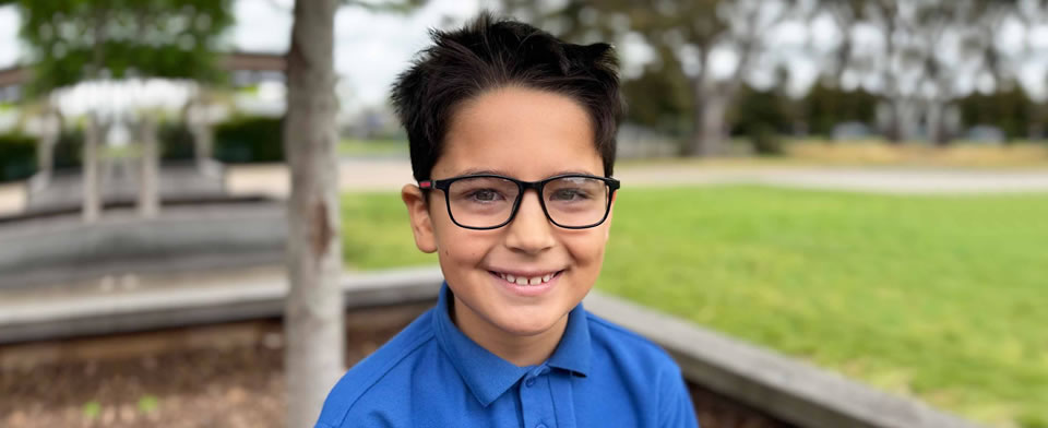 Boy standing outside in park smiling with glasses