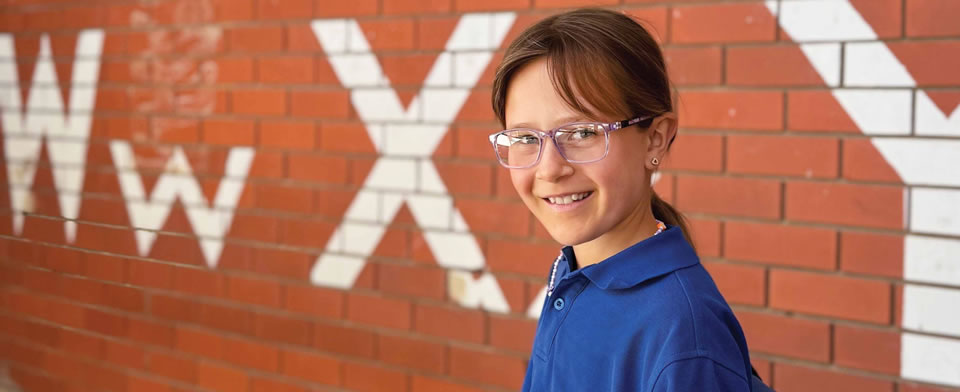 Girl with glasses standing infront of brick wall with writing